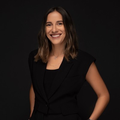 Mujer vestida con traje negro y camisa negra, de pie con una expresión seria.